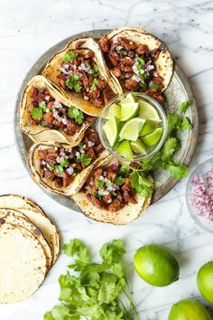 several tacos on a plate with limes, cilantro and other ingredients