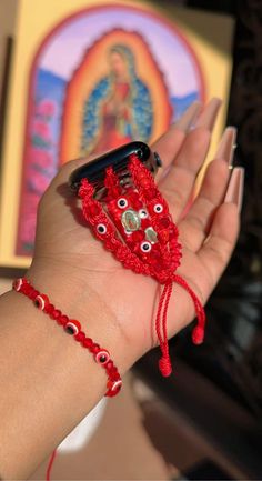 a woman's hand holding a cell phone with beads on it and a red bracelet around her wrist