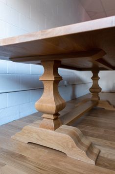 a wooden table sitting on top of a hard wood floor next to a white brick wall