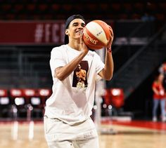 a young man holding a basketball in his right hand and wearing a white t - shirt