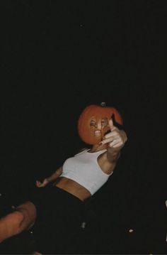 a woman wearing a fake pumpkin hat on top of her head and pointing to the side