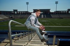 a young man sitting on the bleachers at a football stadium holding a football