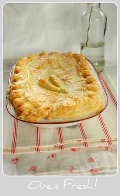 a pie sitting on top of a red and white table cloth next to a glass bottle