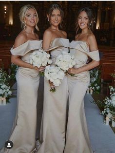 three beautiful women standing next to each other in front of a pewed church aisle