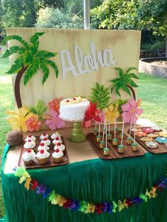 a table topped with lots of cupcakes next to a sign that says aloha