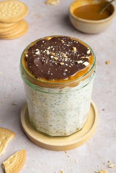 a glass jar filled with pudding and topped with chocolate frosting next to some cookies