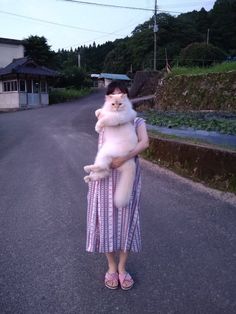 a woman holding a cat in her arms while standing on the side of a road