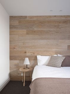 a bed sitting in a bedroom next to a wooden wall with two lamps on each side