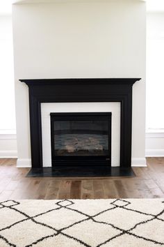 a white fireplace with a black mantle in the middle and a rug on the floor next to it