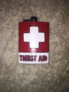 a red and white flask with the words first aid on it sitting on a carpet