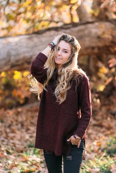 a woman in black jeans and a maroon sweater smiles while standing on the ground with her hands behind her head