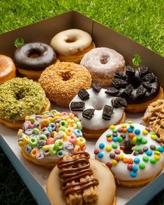 a box filled with different flavored donuts on top of green grass and covered in sprinkles