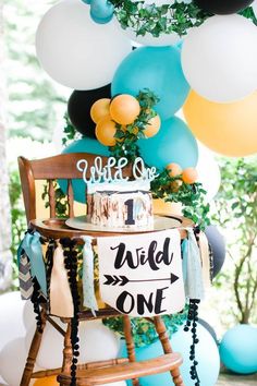 a table topped with balloons and a cake on top of a wooden chair next to a sign