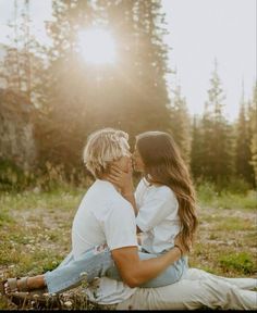 a man and woman sitting on the ground in front of some trees with sun shining behind them