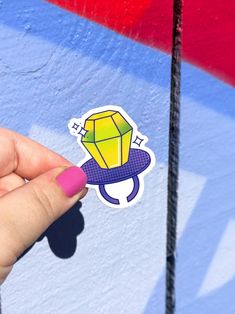 a hand holding a sticker with a diamond on it in front of a painted wall