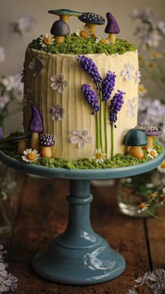 a cake decorated with lavenders and mushrooms on a blue pedestal next to flowers in vases