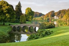 a stone bridge over a river in the middle of a lush green park with lots of trees