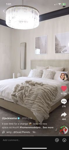 a white bed sitting under a chandelier next to a wall with pictures on it