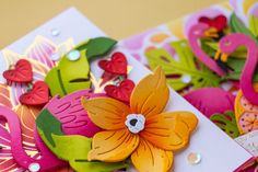 some paper flowers are sitting on top of each other and one is pink, orange, yellow and green