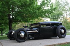 an old black car is parked on the side of the road in front of some trees