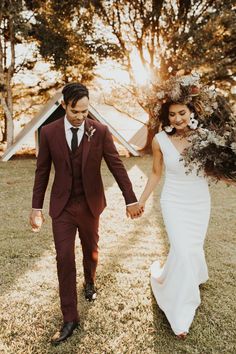 a bride and groom holding hands walking through the grass