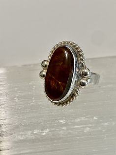 "Mexican Fire Agate set in Sterling Silver with a southwestern design work. The Fire Agate is a natural stone with a dark brown base color and bubbles of \"Fire\". This beautiful stone measures 19 mm by 10 mm. It is bezel set in Sterling Silver and has a rope design setting. The ring is measures 21mm long x 17mm wide. The band tapers to 4 mm Size- 7 Marked- none (tested and confirmed sterling Silver) Weight-4.58g" Artisan Brown Gemstone Rings, Brown Oval Cabochon Rings, Unique Brown Oval Rings, Brown Oval Agate Rings, Oval Brown Agate Rings, Brown Oval Rings With Natural Stones, Oval Brown Rings With Natural Stones, Oval Brown Ring With Natural Stones, Fire Agate Ring