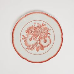 a red and white plate with flowers on the rim is sitting on a white surface