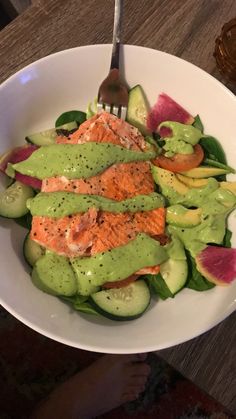 a white bowl filled with salmon and cucumber on top of a wooden table