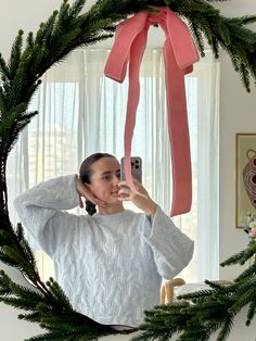 a woman taking a selfie in front of a christmas wreath with a pink ribbon