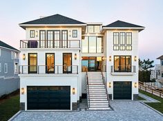 a two story white house with black garage doors and steps leading up to the second floor