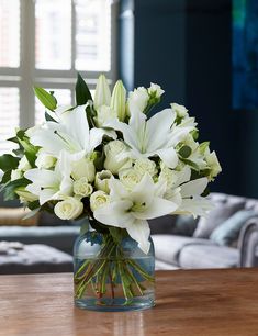 a vase filled with white flowers sitting on top of a wooden table next to a couch