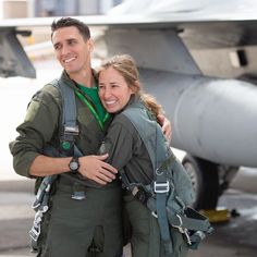 a man and woman are standing in front of an airplane with their arms around each other