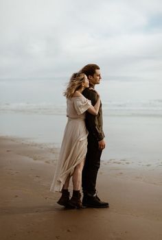 a man and woman standing next to each other on top of a sandy beach near the ocean