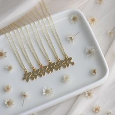 four pieces of gold puzzle necklaces on a white plate with flowers in the background