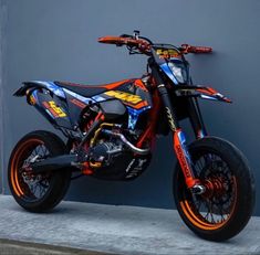 an orange and blue dirt bike parked next to a wall