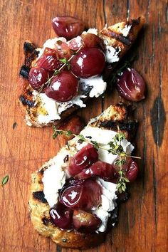 three pieces of bread with cheese and cherries on them sitting on a wooden table