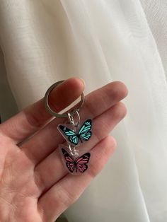 a hand holding a keychain with two butterflies on it's front and back