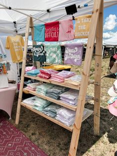 an outdoor market with t - shirts and other items for sale under a tented area