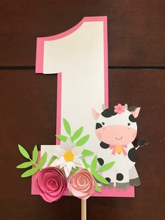 a cake topper with a cow on it and flowers in front of the number one