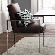 a brown leather chair sitting in front of a table with a pillow on top of it