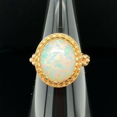 The 4.30 carat opal in this handmade 18k yellow gold ring is bursting with color! This gemstone displays flashes of bright green, orange, yellow, and the most highly-prized and rare color: red! It is difficult for photos to do this opal justice. This ring was custom-designed by our Master Jewelers in Los Angeles in order to showcase the high dome, depth of color and life in this gem. The sides of the ring have been hand engraved and show a level of artisanship and skill seldom seen today. A ring Yellow Gold Opal Ring With Cabochon, Yellow Gold Ethiopian Opal Ring In Oval Shape, Yellow Gold Ethiopian Opal Ring In Oval Cabochon Shape, Yellow Gold Ethiopian Opal Oval Cabochon Ring, Ethiopian Opal Oval Cabochon Ring In Yellow Gold, Collectible Yellow Gold Opal Ring Oval Cabochon, Collectible Oval Cabochon Opal Ring In Yellow Gold, Yellow Gold Cabochon Opal Ring Collectible, Yellow Gold Cabochon Opal Ring For Collectors