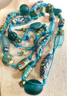 A beautiful combination of Ghana Krobo beads are hand-knotted to create this long necklace.  It is a one-of-a-kind piece. -  Handmade, one-of-a-kind. -  Lovely combination of teal and yellow Ghana Krobo beads, sandcast, fused glass, ceramic, and recycled glass beads. -  The hand-knotting and spacing allows for each bead to be individually showcased. -  Necklace measures 36" in length and is not adjustable. -  Beads are strung on teal hemp cord. -  Brass "hand made" charm tag. -  Comes with jewel Bohemian Hand-strung Necklaces For Festivals, Bohemian Festival Hand-strung Necklaces, Unique Recycled Glass Necklaces For Beach, Unique Recycled Glass Beach Necklace, Bohemian Adjustable Recycled Glass Necklace, Bohemian Adjustable Necklace With Recycled Glass, Adjustable Bohemian Necklace With Recycled Glass, Hippie Style Green Beaded Necklace For Festivals, Artisan Adjustable Recycled Glass Necklace