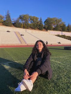 a woman sitting on the ground in front of an empty stadium