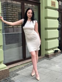 a woman in a short white dress is standing on the sidewalk near a storefront