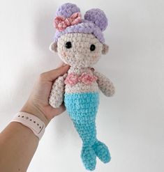 a crocheted mermaid doll being held by a person's hand on a white background