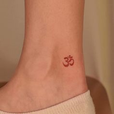 a small tattoo on the ankle of a woman with an omen symbol in red ink