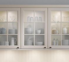 a kitchen cabinet with glass doors and dishes on the bottom shelf in front of it