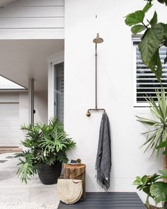 an outdoor shower with plants and a towel hanging on it's side wall in front of a white house