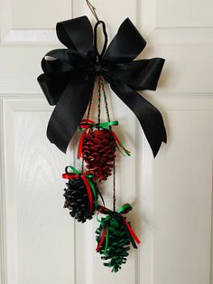 three pine cones hanging from a door with black ribbon and bells attached to the front