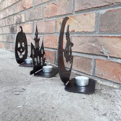 three metal sculptures sitting on the side of a brick wall next to a candle holder